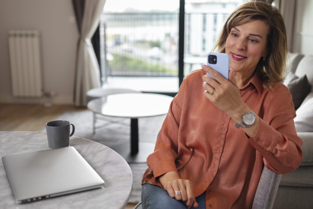 A woman using her phone while enjoying a cup of coffee in her new home in the concept of 'how to settle into a new home after moving to Canary Wharf'.