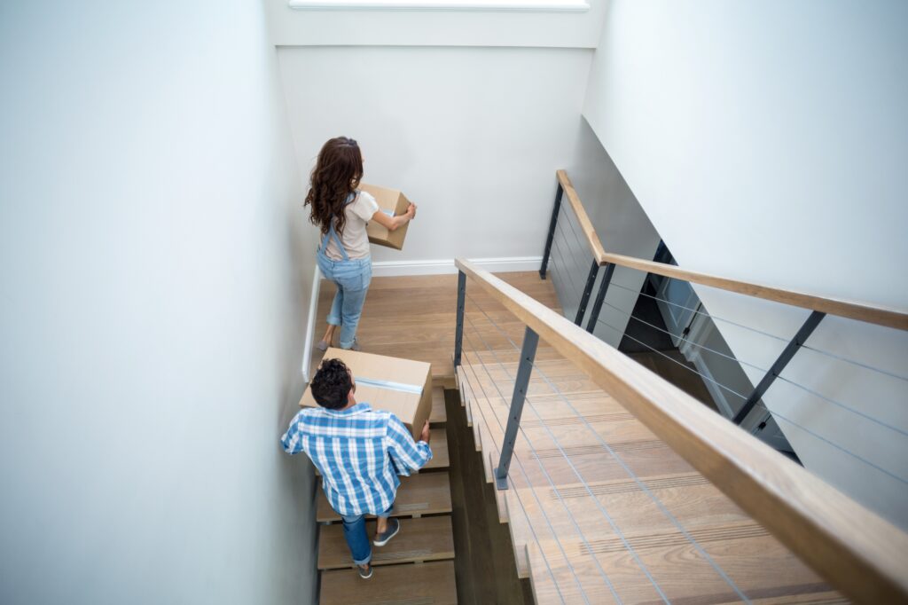A couple climbing a narrow staircase while carrying boxes on the moving day
