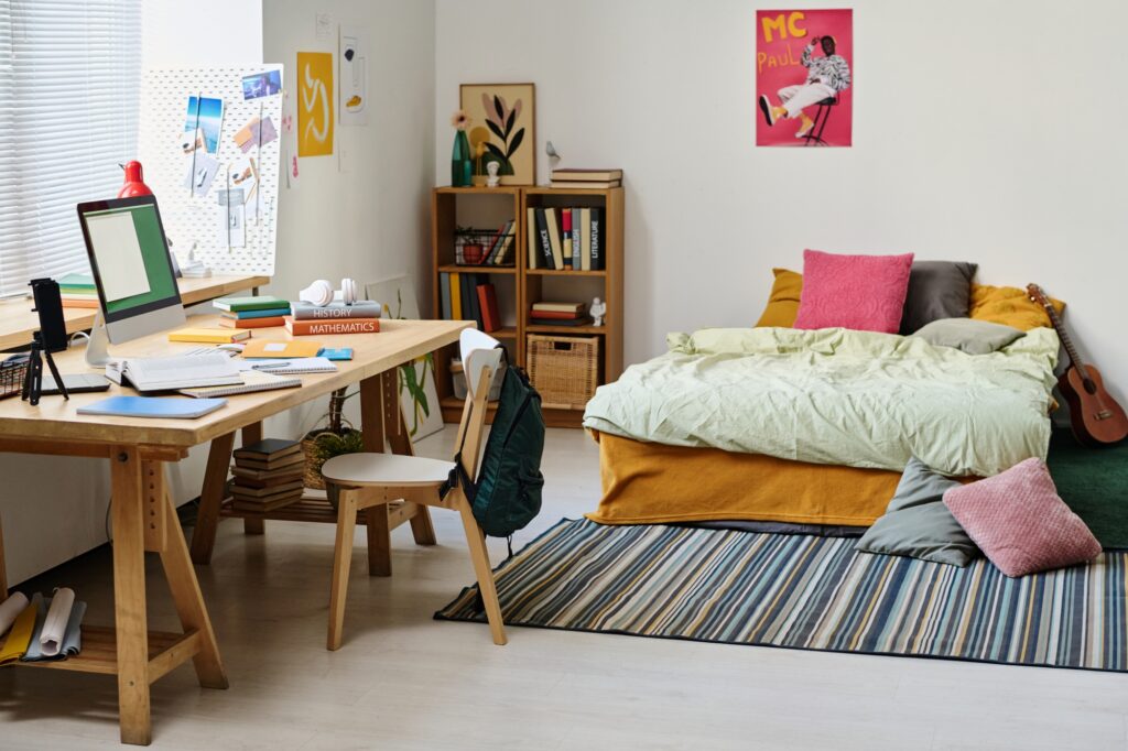 A student's dorm room with bed, pillows, books, desk, chair, and computer